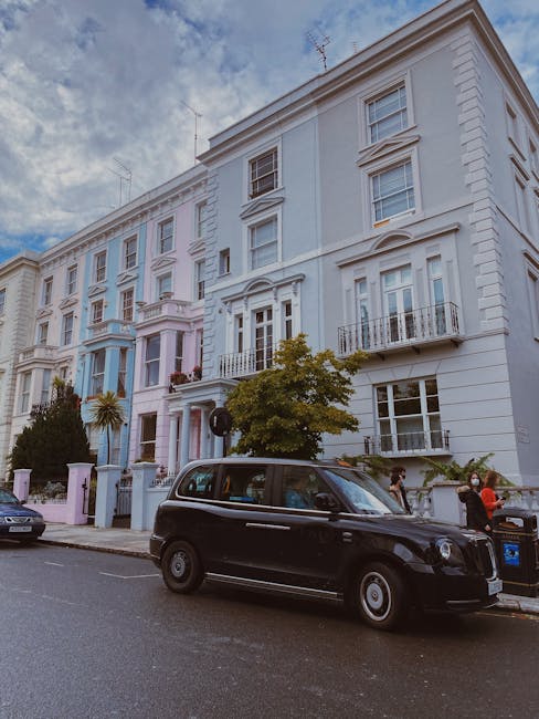 A black bicycle with orange reflectors on the wheels is parked against a black metal fence in front of a teal and cream-coloured Victorian-style townhouse with sash windows and a stone-flagged entranc